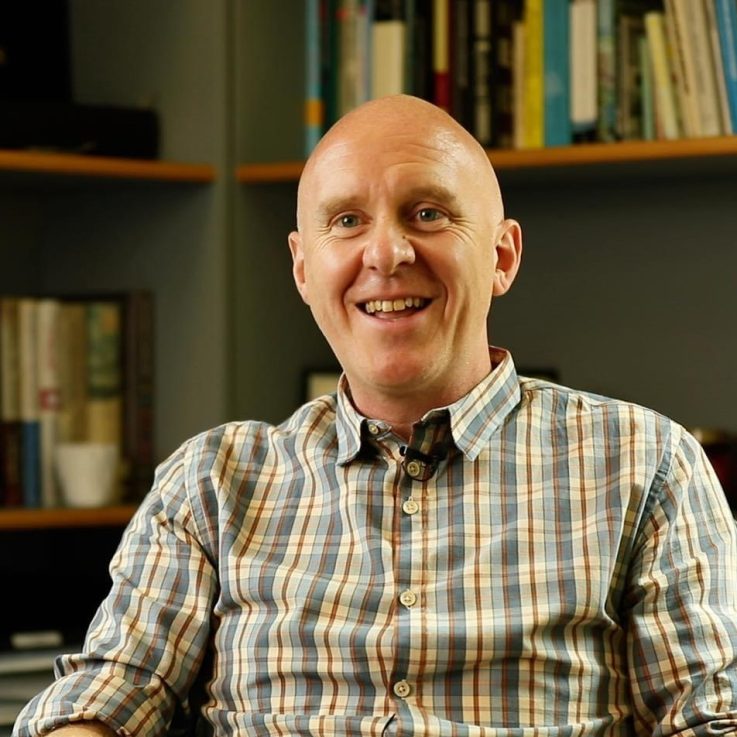 A head and shoulders photo of Matthew Taylor sitting in front of a bookcase in his office.