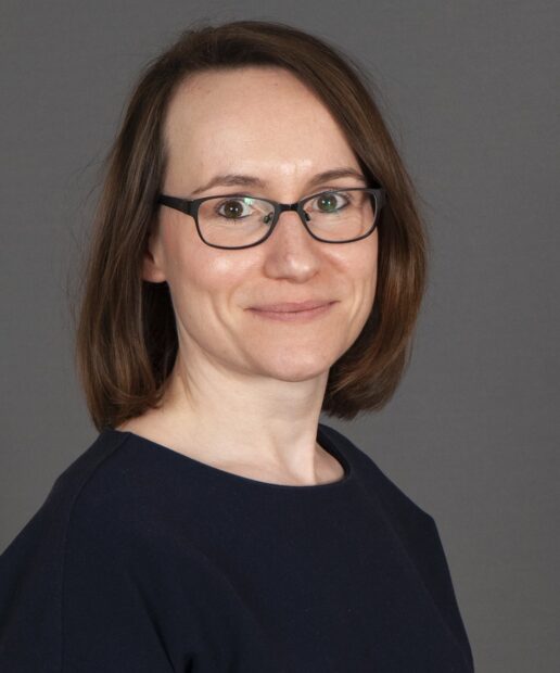 A head-and-shoulders photo of Beth Woods smiling at the camera against a dark background