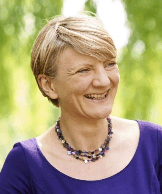 A photo of Karen Bloor smiling at someone off camera. She is standing outside on a sunny day, with trees in the background.