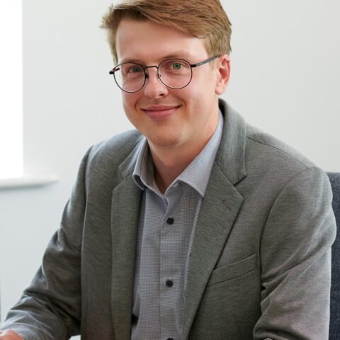 Joe Moss sitting at a desk, smiling at the camera