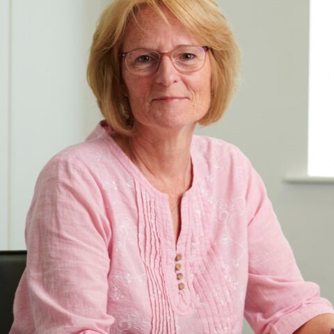 Jo Hanlon sitting down at a desk, smiling at a camera.