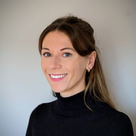 A head-and-shoulders photo of Emily Gregg smiling at the camera, against a neutral background