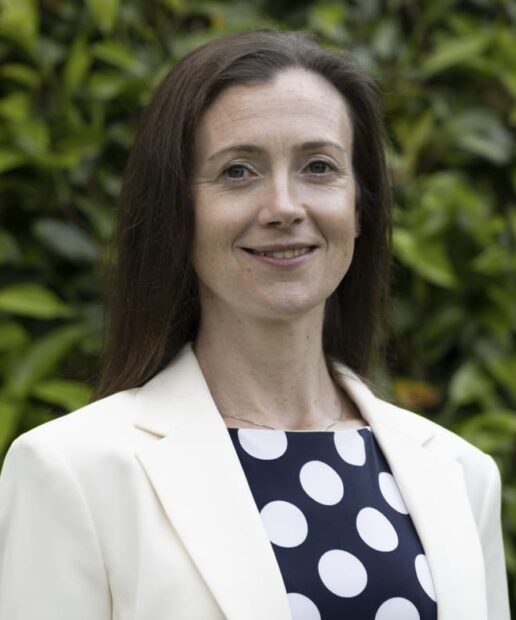 A head-and-shoulders photo of Mary Jordan, who is smiling at the camera. She is stood outside, with greenery visible behind her.