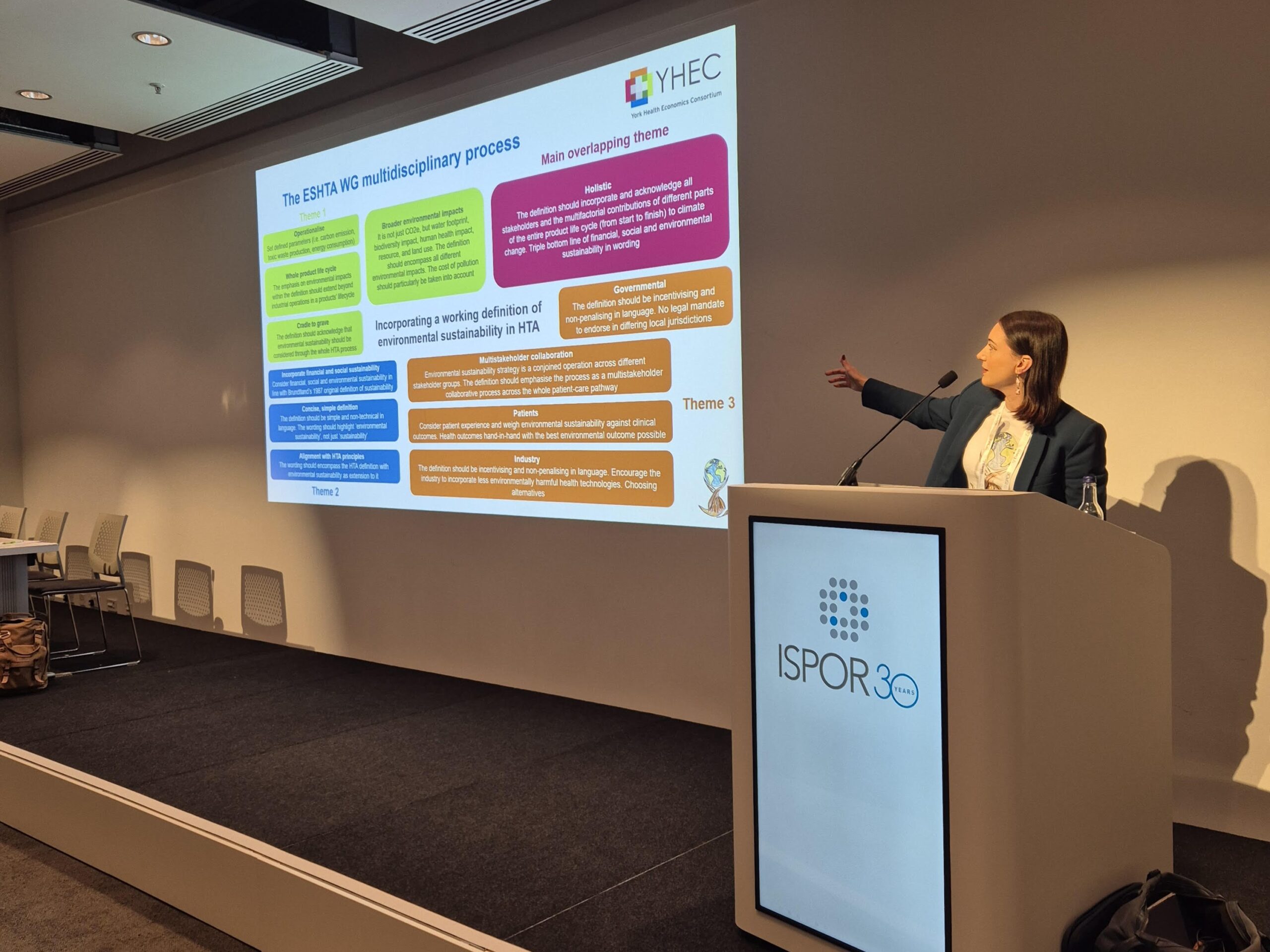 Melissa Pegg is leading a panel presentation, gesturing towards the slides displayed next to her.