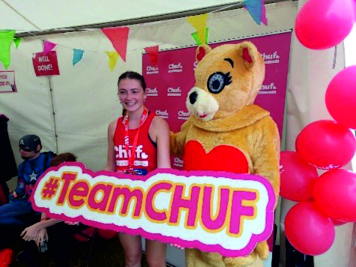 An image of a YHEC staff member who took part in the Great North Run. In the image, they are with the Children's Heart Unit Fund mascot and holding a sign that reads: "#TeamCHUF"